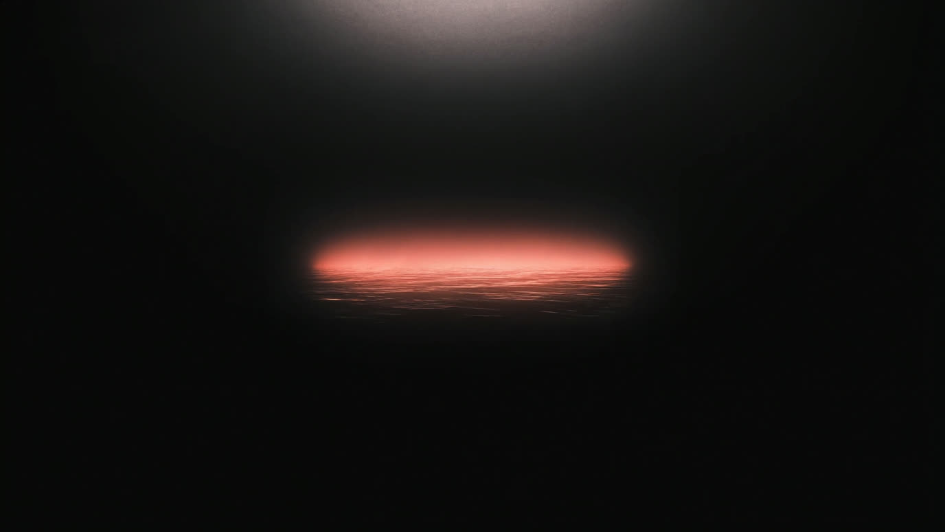 Soft warm coral light rising like dawn over calm dark water, out of deep ink-black.