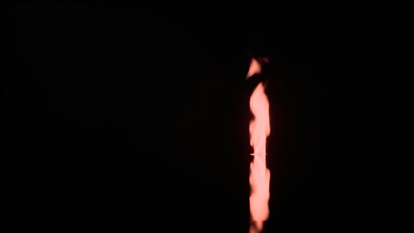 A single steady coral flame reflected on still, dark water.